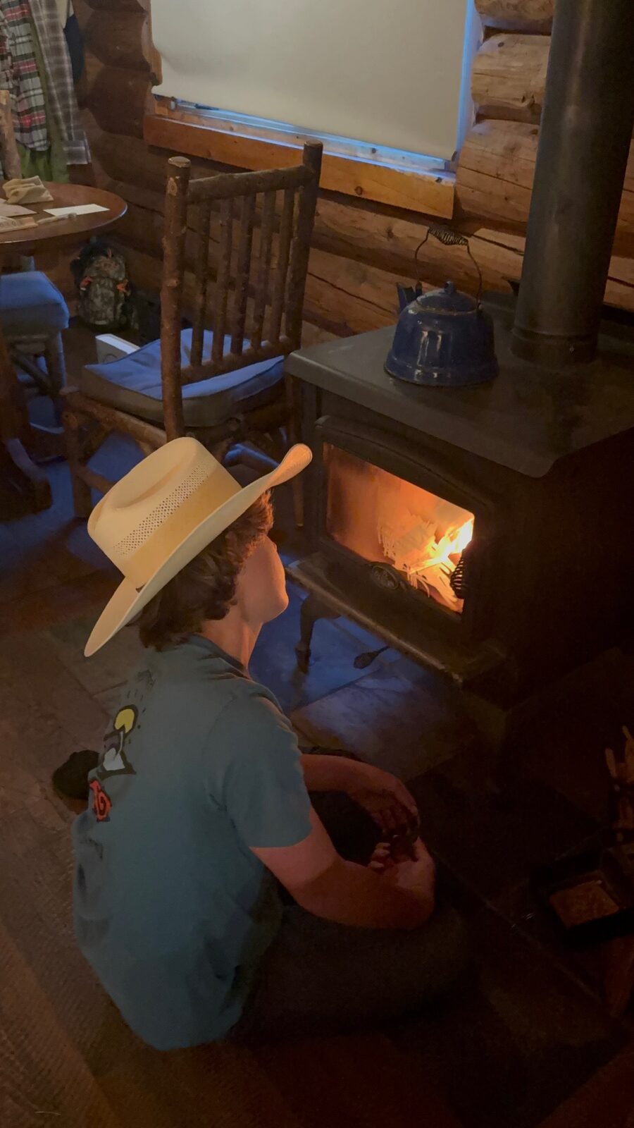 Dylan in a cowboy hat sitting by the cabin wood stove