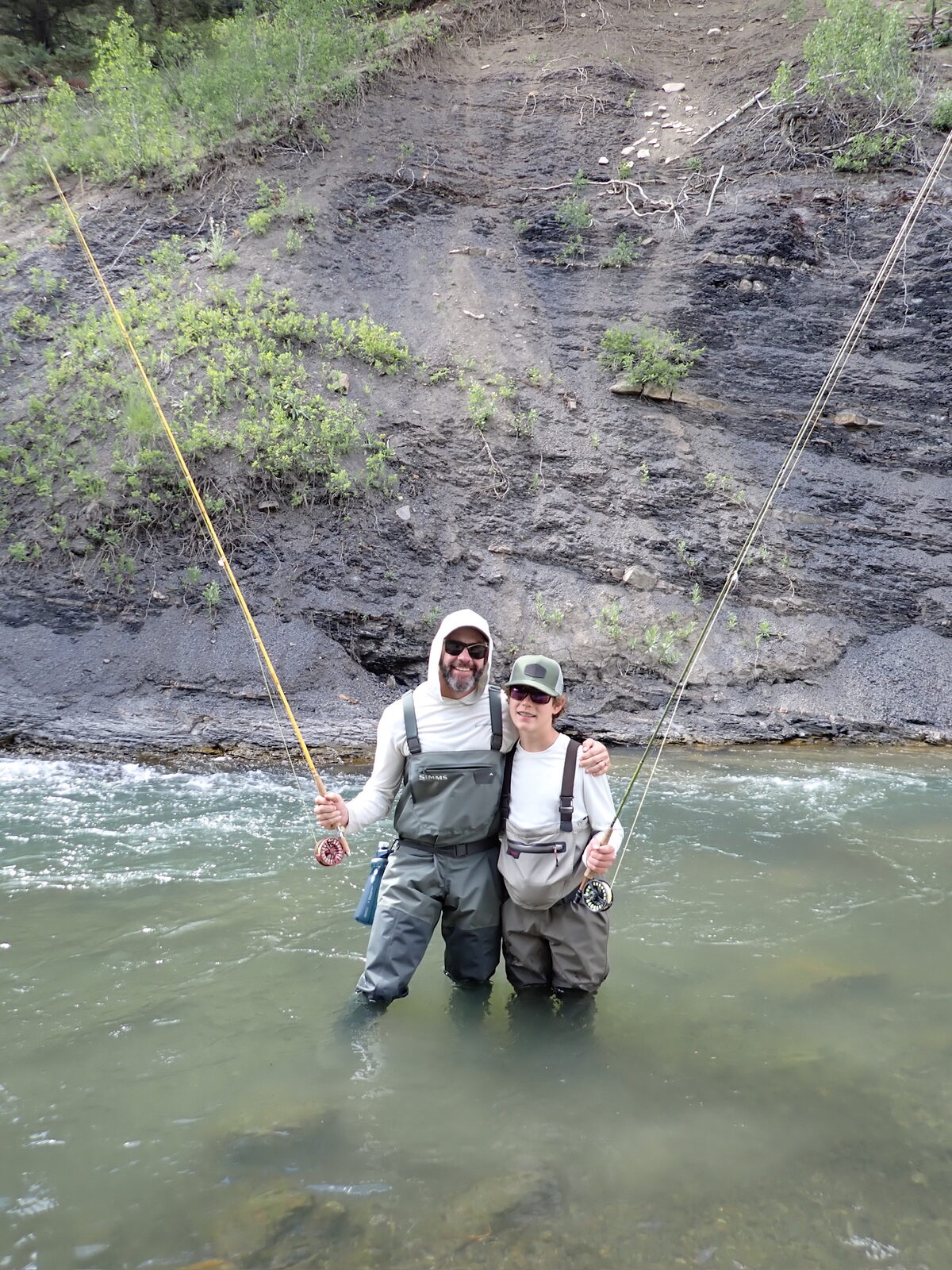 Mark and Dylan in waders standing in the river with rods